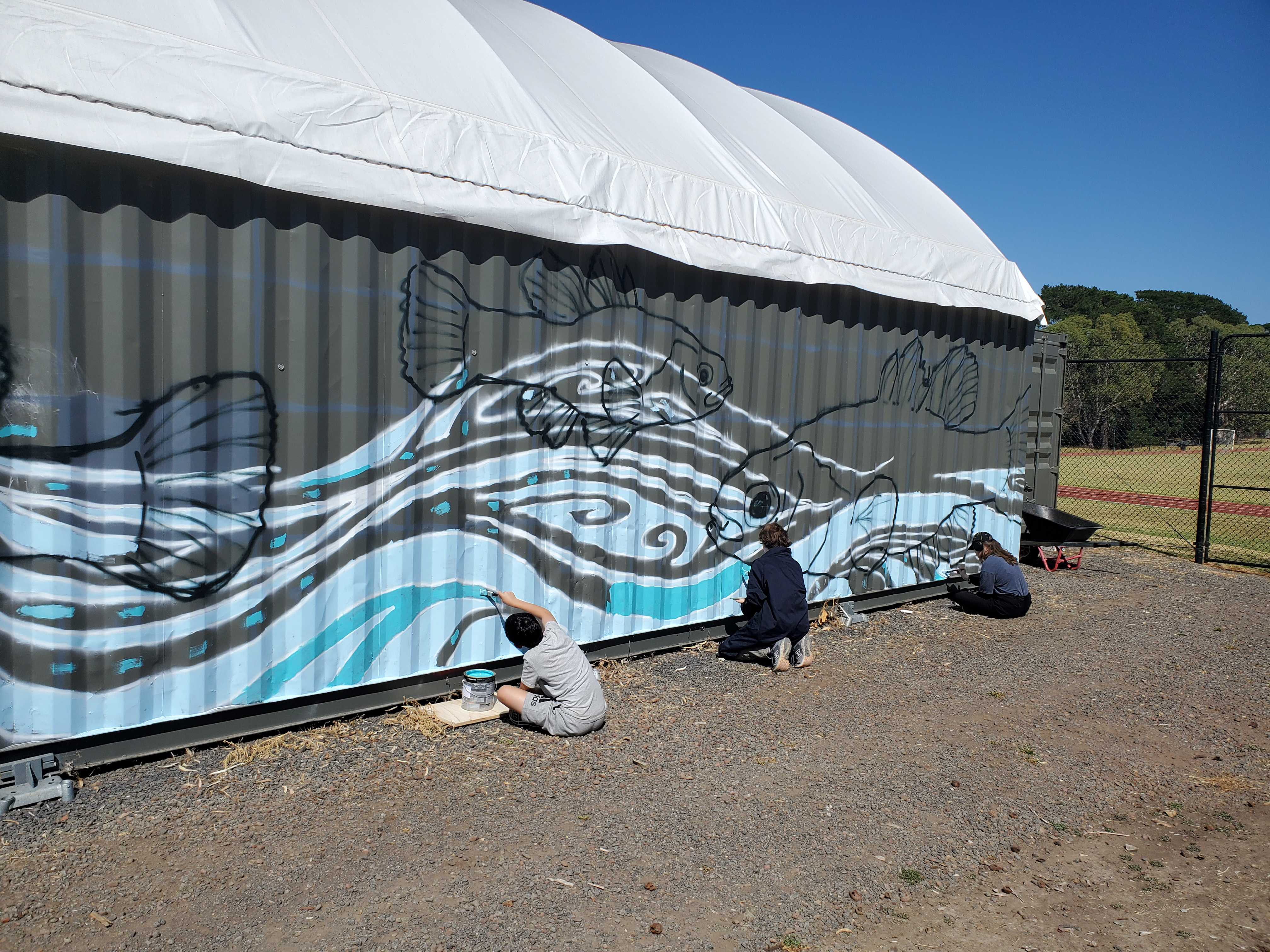 Three students painting a mural on a grey building
