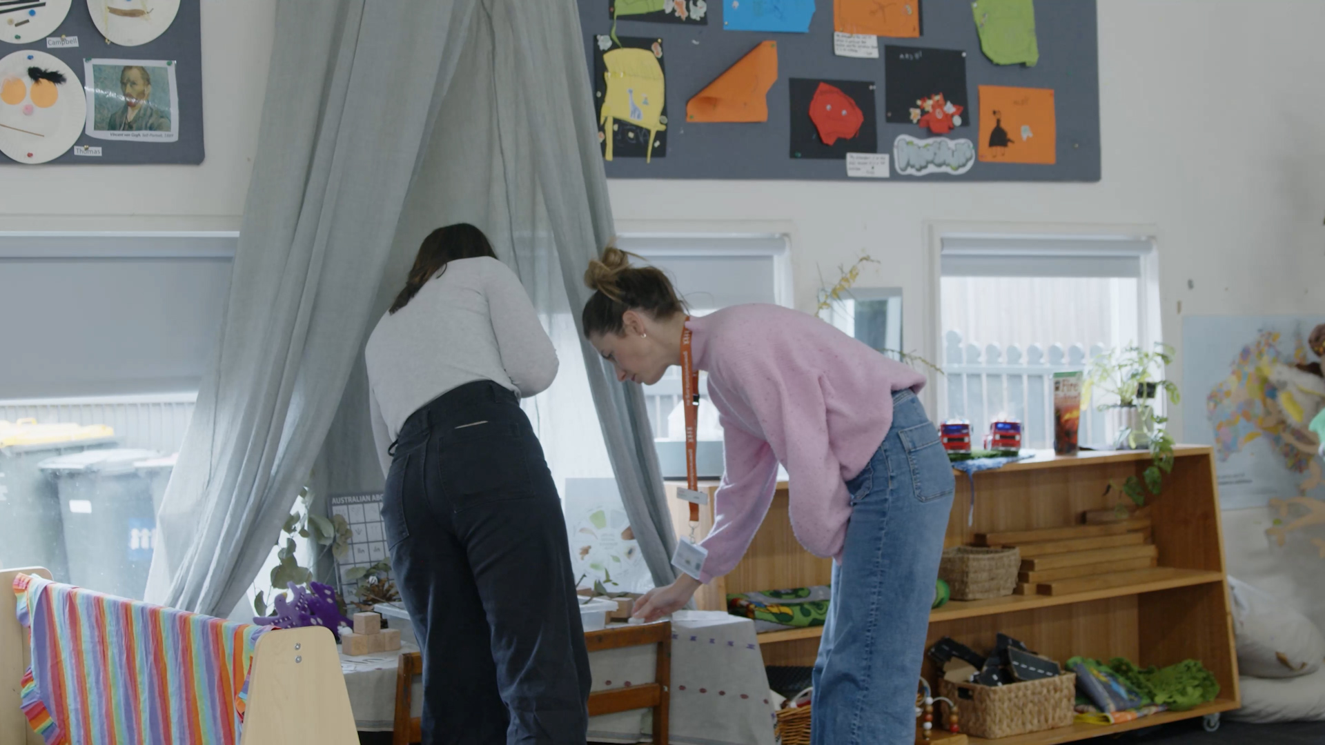 Two teachers leaning down and looking at something on a table