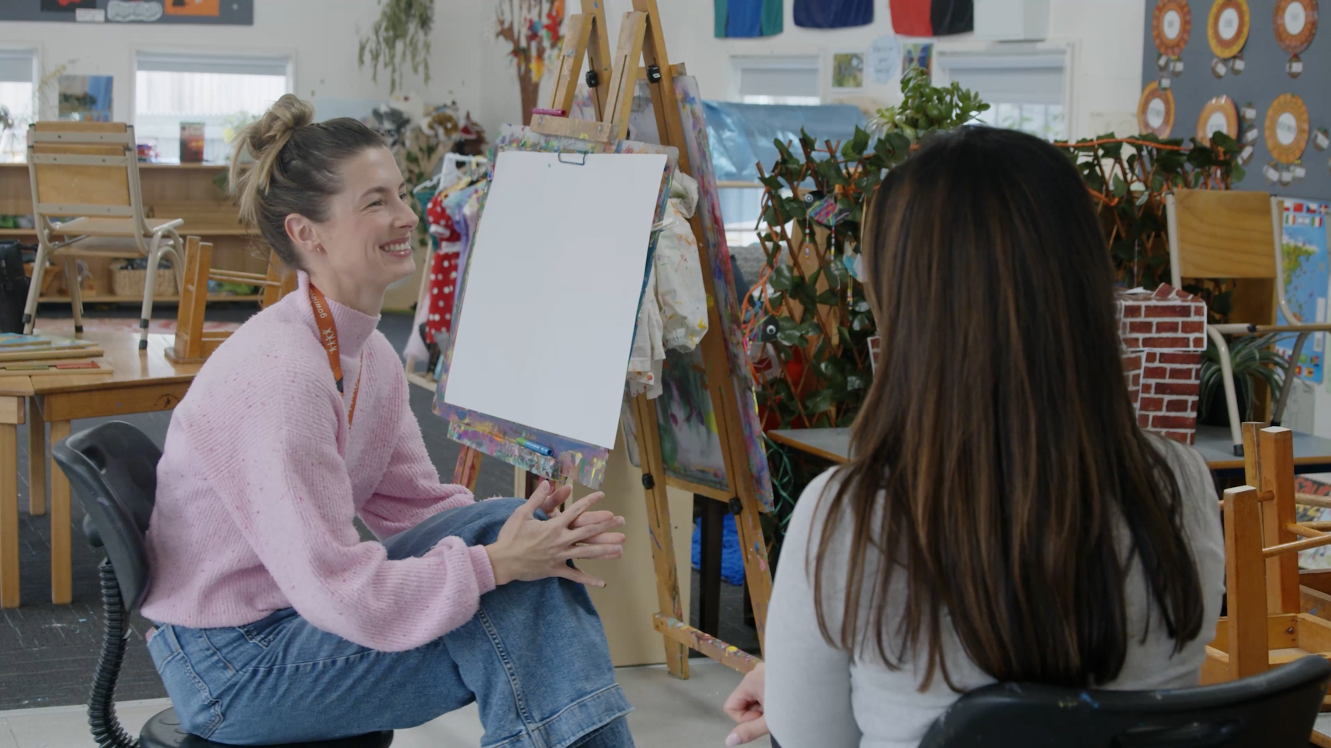 Teacher sitting down with another teaching in an art room