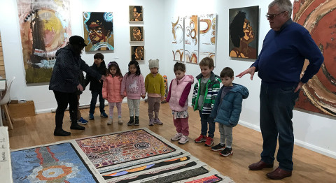 A group of children with Glenn Louhrey, looking at Aboriginal artworks laid out on the floor.
