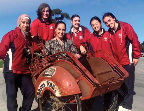 A teacher and group of students, smiling at the camera