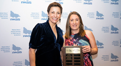 Two people smile at the camera, standing in front of a media wall at the PASS Awards