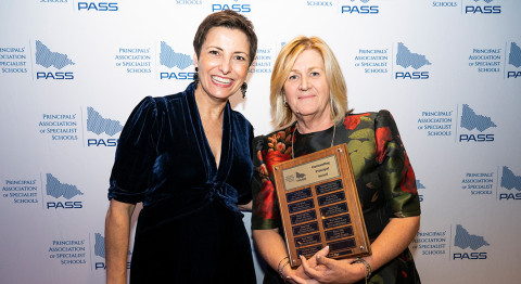 Two people smile at the camera, standing in front of a media wall at the PASS Awards