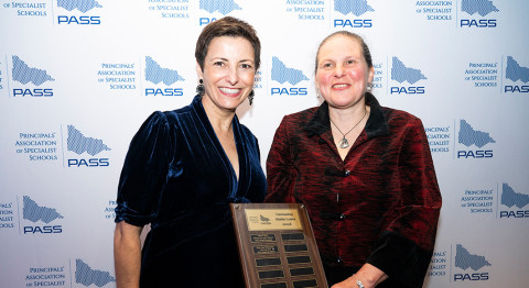 Two people smile at the camera, standing in front of a media wall at the PASS Awards