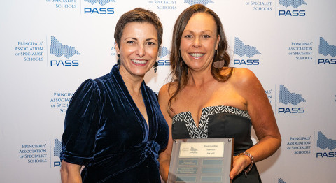 Two people smile at the camera, standing in front of a media wall at the PASS Awards