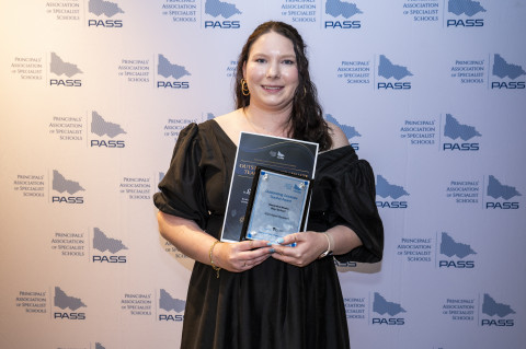 Image of teacher holding awards, smiling at the camera