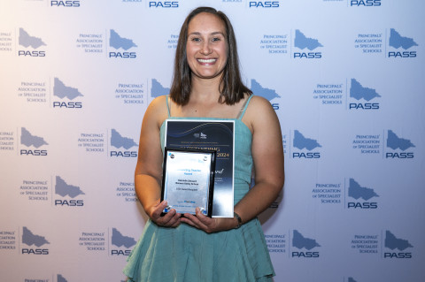 Image of teacher holding awards, smiling at the camera