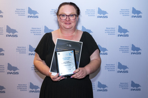 Image of teacher holding awards, smiling at the camera