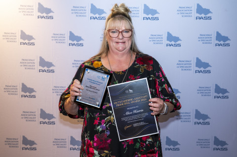 Image of teacher holding awards, smiling at the camera