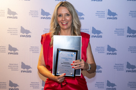 Image of teacher holding awards, smiling at the camera